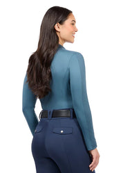 Woman wearing teal long sleeve riding shirt with riding tights, rear view