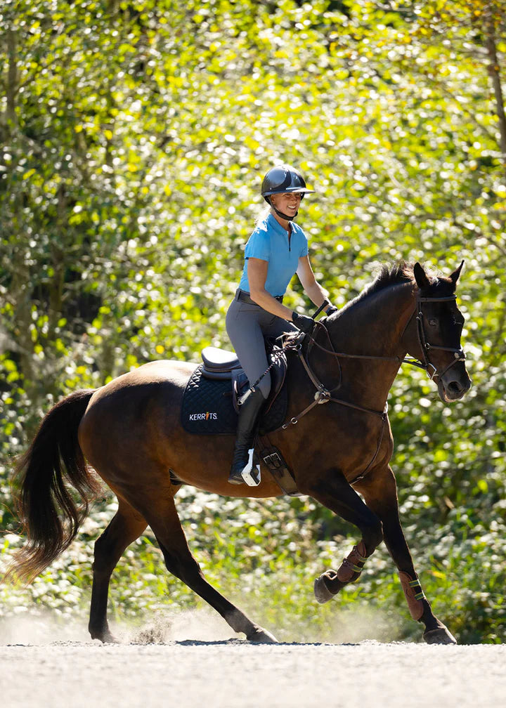Rider wearing a bright blue polo shirt riding a horse outdoors