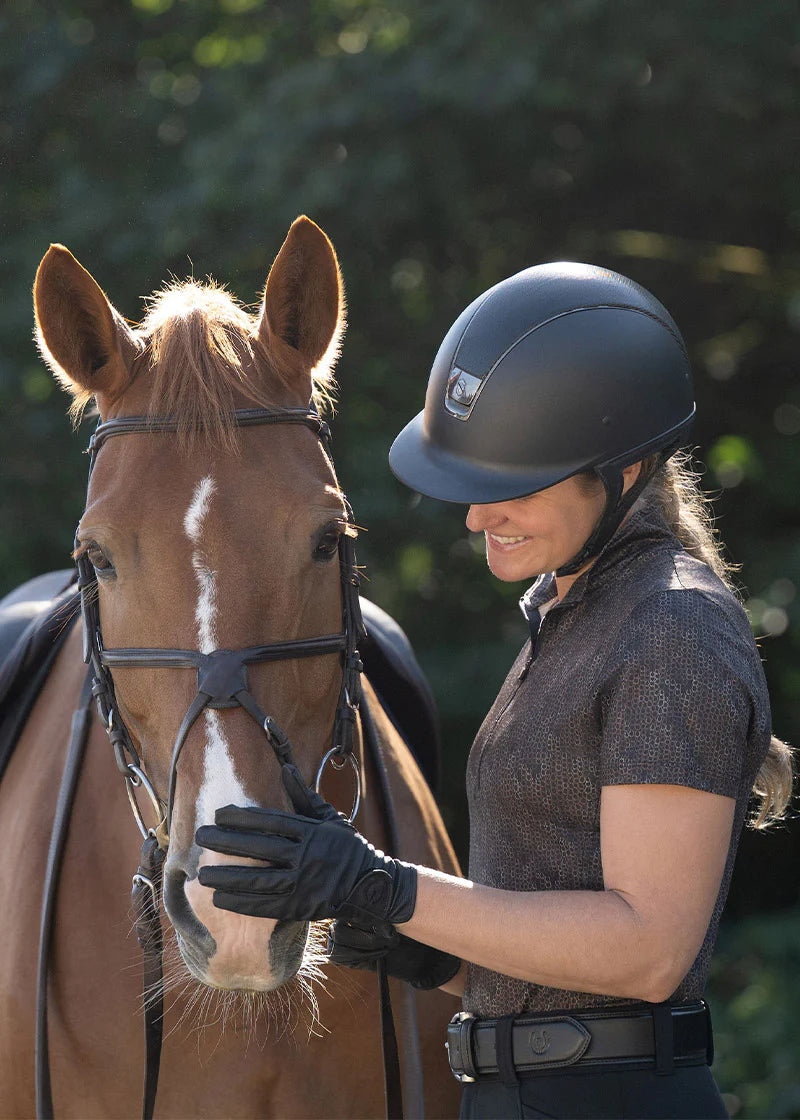 Woman wearing a brown riding shirt standing beside a horse
