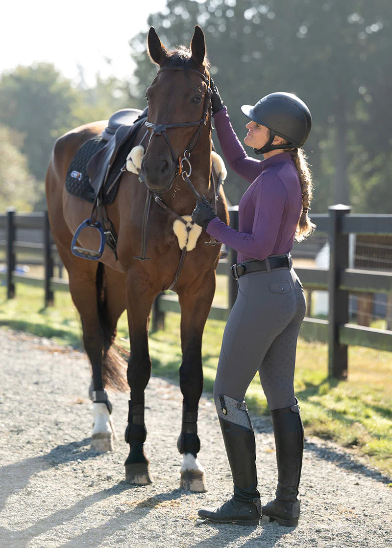 Side view of a female model wearing the gray Kerrits Free Motion Coolcore Full Seat Breech while petting a bay horse