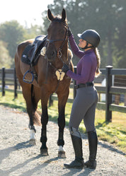 Side view of a female model wearing the gray Kerrits Free Motion Coolcore Full Seat Breech while petting a bay horse