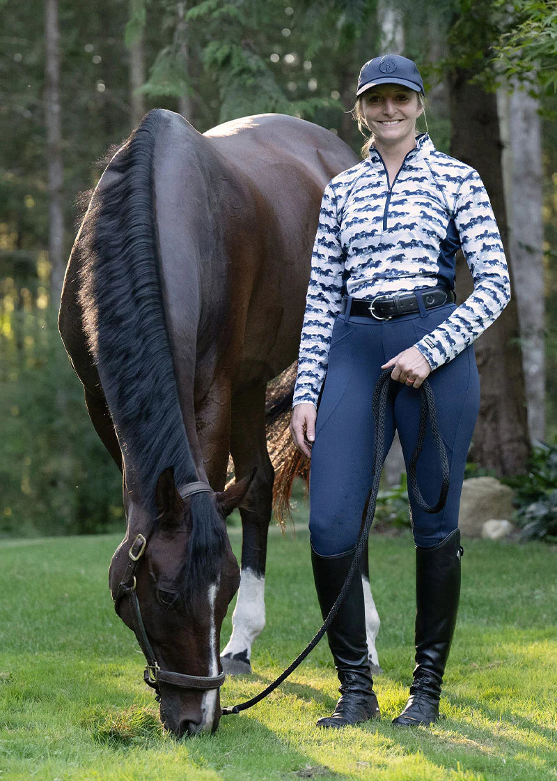 Woman standing beside a horse wearing a horse print riding shirt