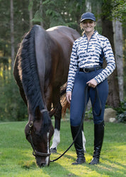 Woman standing beside a horse wearing a horse print riding shirt