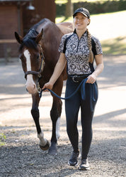 Woman leading a horse while wearing a patterned riding shirt