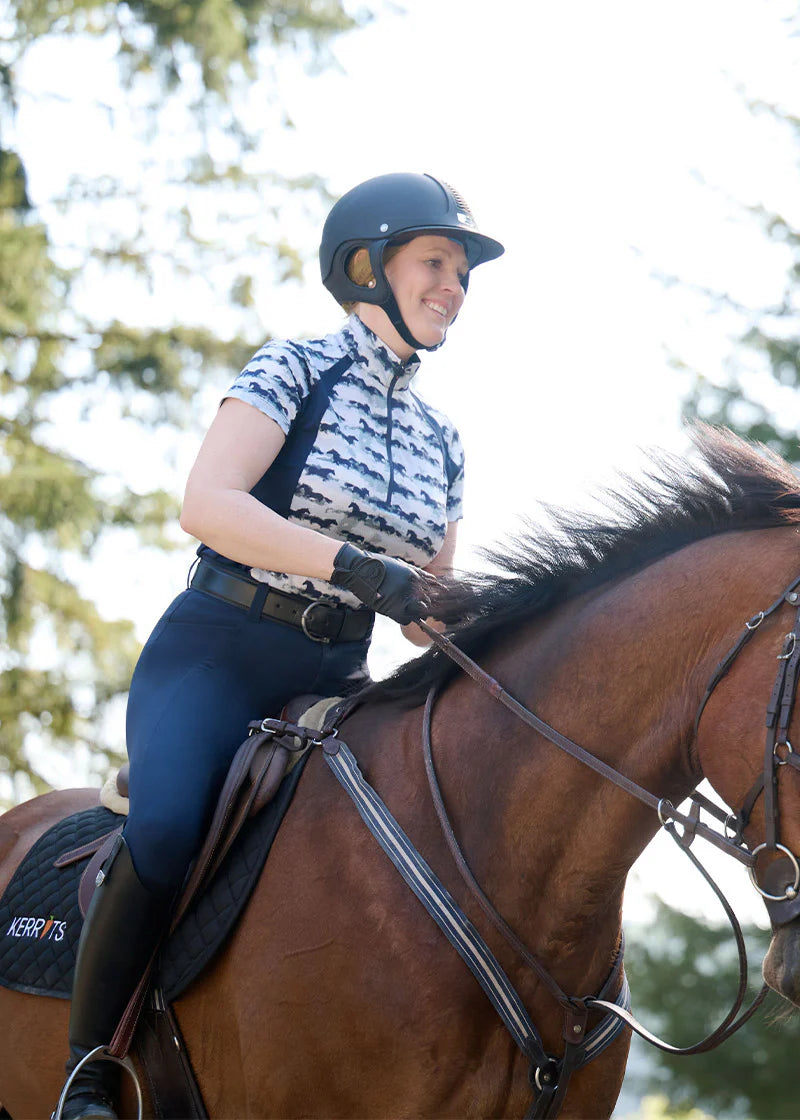 Rider wearing a horse print shirt riding a horse