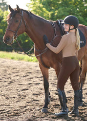 Woman standing with a horse wearing brown riding tights