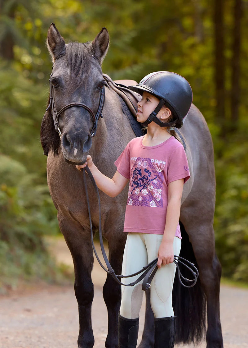 Front view of a young female model wearing the Tan Kerrits Kids Performance Knee Patch Pocket Tight while standing next to a pony