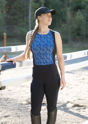 Woman standing outdoors wearing black riding tights and a blue sleeveless top