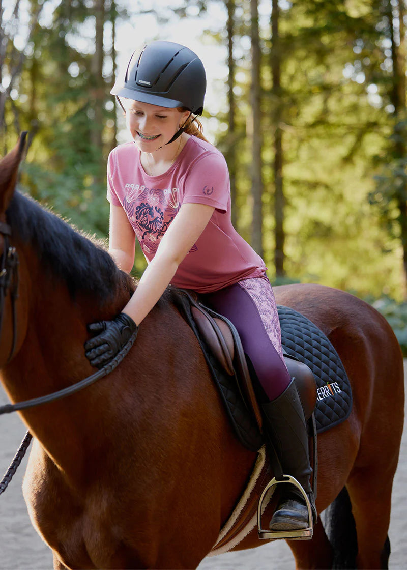 Front view of a young female model wearing the purple Kerrits Kids Performance Knee Patch Riding Tight while riding a bay horse