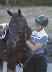 Woman standing next to a horse while wearing light blue short sleeve riding shirt with white stripe detail