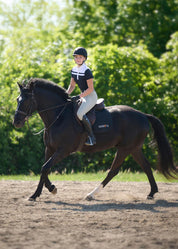 Full view of rider wearing black short sleeve riding shirt with white stripe detail riding a horse outdoors