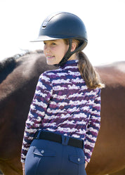 Back view of a young female model wearing the purple Kerrits Kids EquiBreeze Ice Fil Long Sleeve Shirt while standing in front of a horse