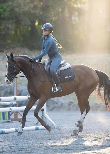 Rider wearing teal long sleeve riding shirt riding a horse outdoors