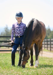 Full body front view of a young female model wearing the purple Kerrits Kids EquiBreeze Ice Fil Long Sleeve Shirt and navy breeches while standing next to a horse