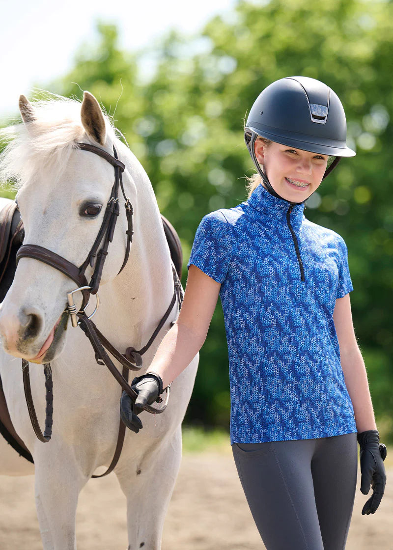 Girl wearing the Kids EquiBreeze Ice Fil Short Sleeve Shirt in the color Oasis Lucky Cascade while standing next to a white horse