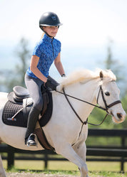 Girl wearing the Kids EquiBreeze Ice Fil Short Sleeve Shirt in the color Oasis Lucky Cascade while riding a white horse