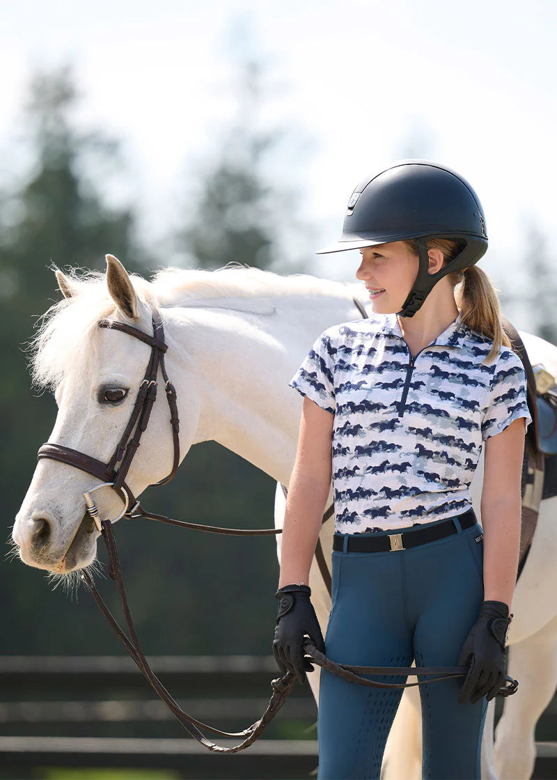 Girl wearing the Kids EquiBreeze Ice Fil Short Sleeve Shirt in Mist Brushstrokes standing next to white horse
