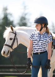 Girl wearing the Kids EquiBreeze Ice Fil Short Sleeve Shirt in Mist Brushstrokes standing next to white horse