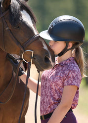 Side view of young female model wearing the pink Kerrits Kids EquiBreeze Ice Fil Short Sleeve Print Shirt while giving a brown horse a kiss on the nose