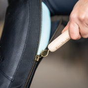 Close-up view of someone using the Kavalkade Wooden Handle Zip Aid to pull up the back zipper on their black tall boot