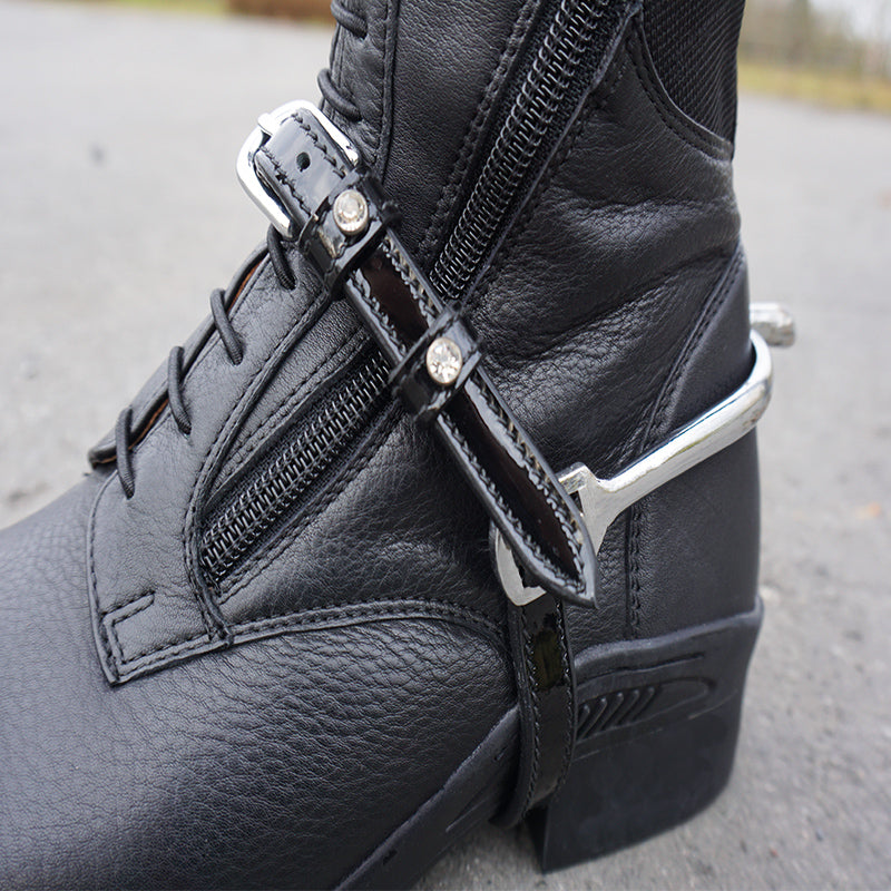Close-up view of the black Kavalkade Crystal Patent Spur Straps over a black boot
