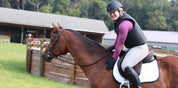 Side view of a woman wearing a Ovation Comfort Flex Body Protector while she is sitting on a bay horse outside