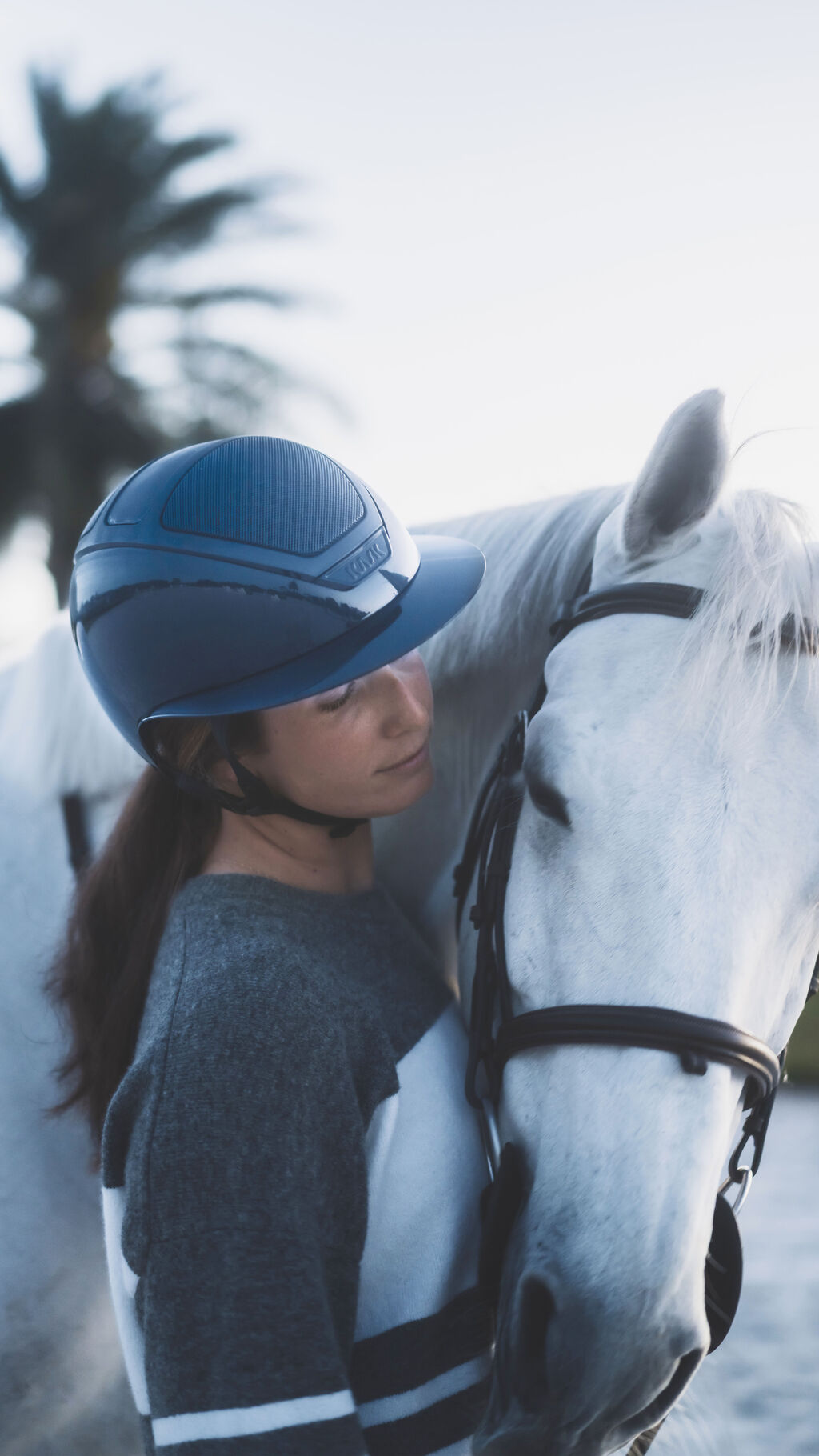 Angled front view of a female model wearing the atlantic KASK Star Lady Pure Shine Helmet while standing next to a gray horse