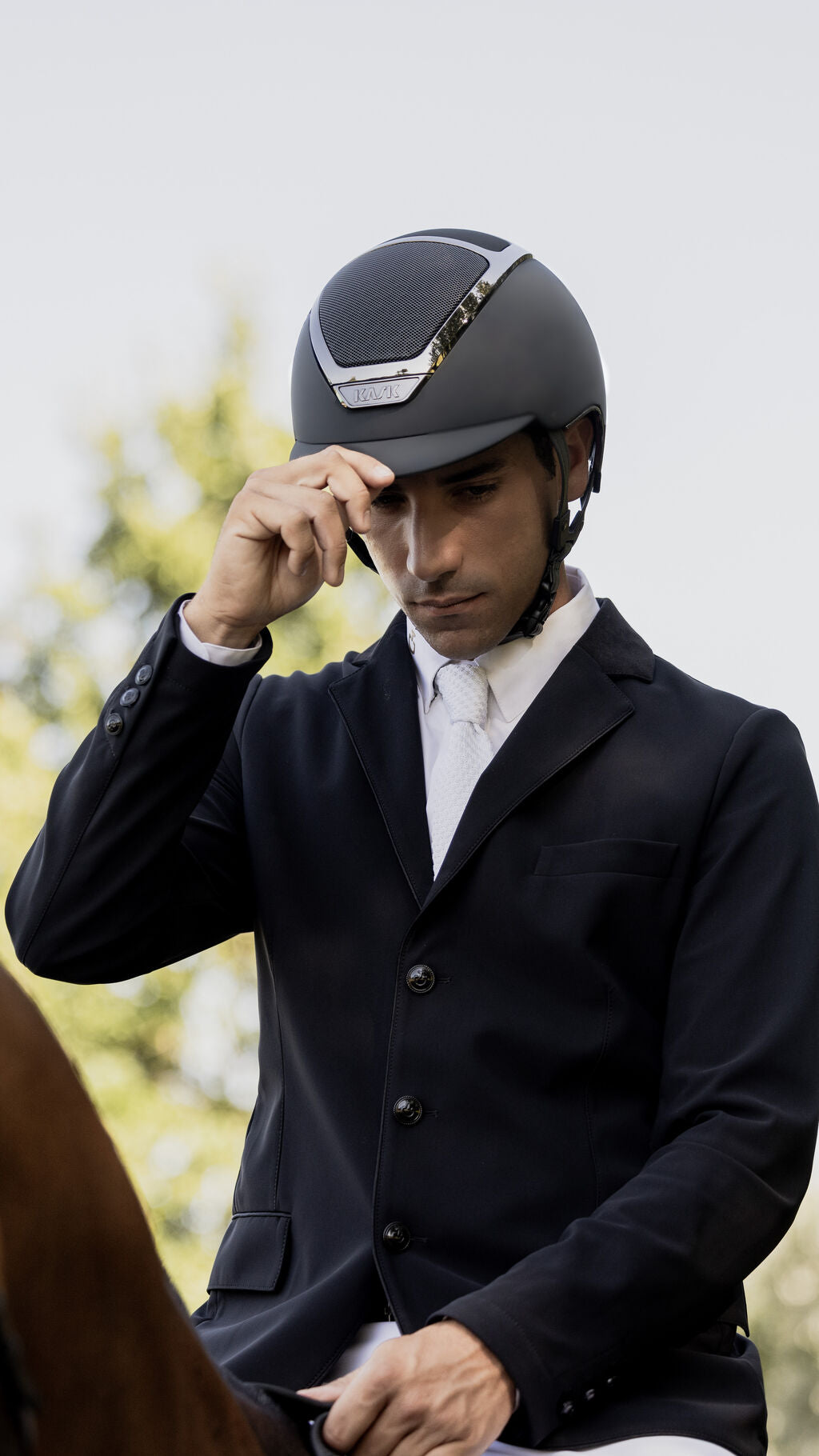 Angled front view of a male rider wearing the anthracite Kask Dogma Chrome Helmet while riding a horse