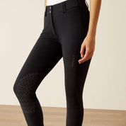 Close-up side view of a model wearing the black Ariat Tri Factor Grip Knee Patch Breech in a studio setting