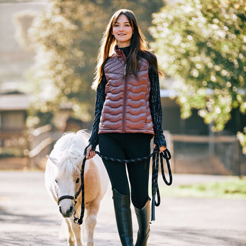 Front view of a female model wearing the black Ariat Tri Factor Grip Knee Patch Breech while walking a miniature pony