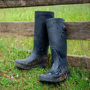 View of a pair of Navy Ariat Kelmarsh Rain Boot leaned up against a wood fence in the grass