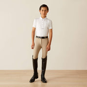 Front view of a young model wearing the Ariat Youth Tek Short Sleeve Show Shirt in white with tan breeches and tall black boots in a studio setting