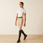 Front view of a youth model wearing the Ariat Aptos Vent 2.0 Show Shirt in white, tan breeches, and black tall boots in a studio setting