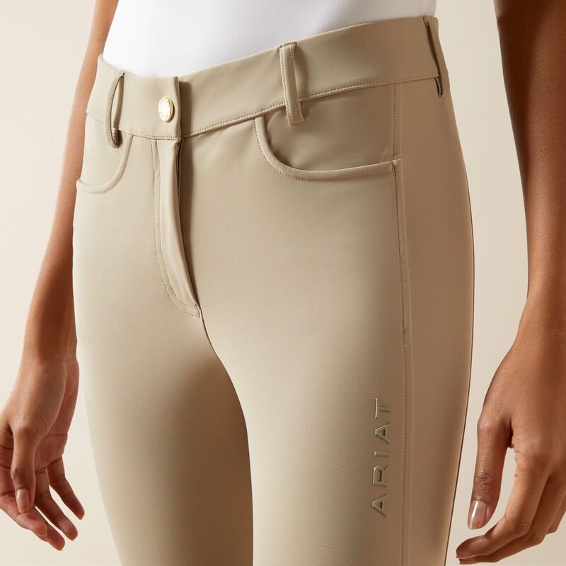 Close-up front view of a model wearing the tan Ariat Tri Factor NT Knee Patch Breech on a plan background