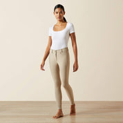 Full body front view of a female model wearing the tan Ariat Tri Factor NT Knee Patch Breech and white shirt in a studio setting