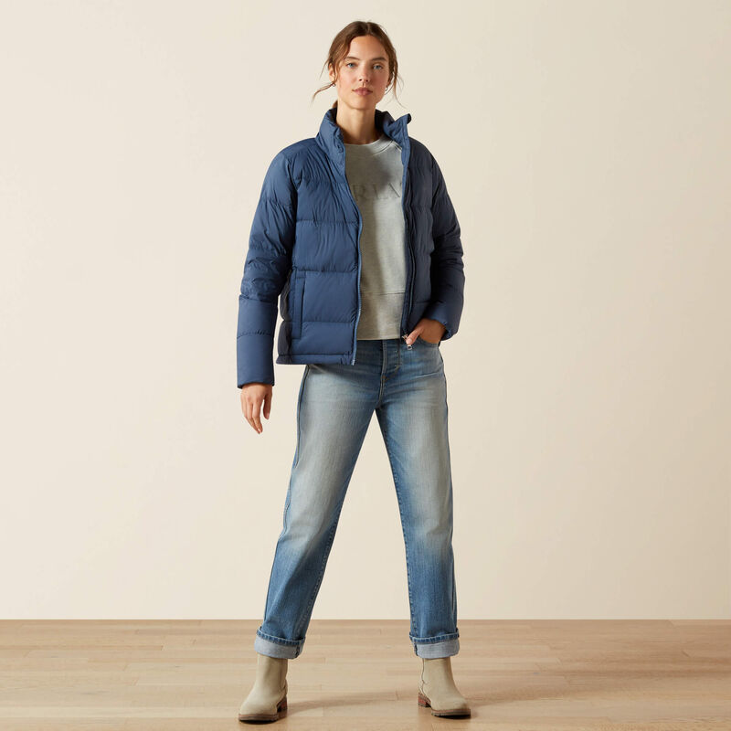 Full body front view of a female model wearing the Big Dipper Ariat Ultrapuff Down Jacket with jeans on a plain background