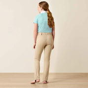 Full body back view of a young girl wearing a blue shirt and the Ariat Youth Protege Jod Knee Patch Breeches in tan in a studio setting