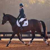 Side view of a female model wearing the Navy Eclipse Ariat Allure Show Coat while riding a bay horse in an outdoor arena