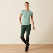 Full front view of a model wearing the Ariat Sustain Short Sleeve Baselayer in green with green breeches and tall black boots in a studio