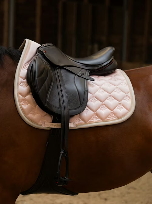 Side view of a bay horse wearing the light pink PS of Sweden Heart Jump Pad under a brown saddle