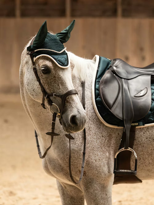 Side view of a gray horse wearing the green PS of Sweden Heart Jump Pad under a brown saddle