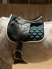 Side view of a gray horse wearing the green PS of Sweden Heart Jump Pad under a brown saddle
