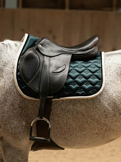 Side view of a gray horse wearing the green PS of Sweden Heart Jump Pad under a brown saddle