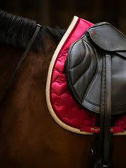 Side view of a bay horse wearing the pink PS of Sweden Heart Jump Pad under a brown saddle