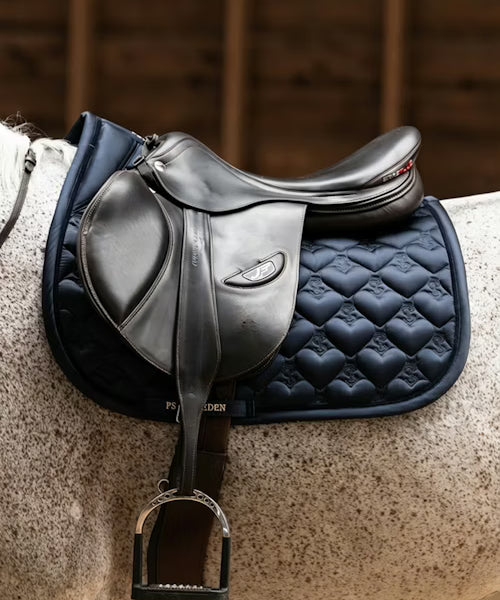 Side view of a gray horse wearing the navy PS of Sweden Heart Jump Pad under a brown saddle