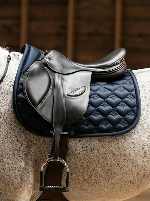 Side view of a gray horse wearing the navy PS of Sweden Heart Jump Pad under a brown saddle