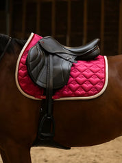 Side view of a bay horse wearing the pink PS of Sweden Heart Jump Pad under a brown saddle