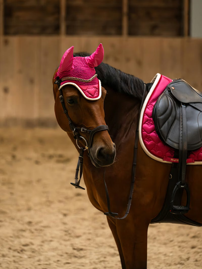 Side view of a bay horse wearing the pink PS of Sweden Heart Jump Pad under a brown saddle