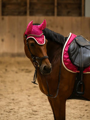 Side view of a bay horse wearing the pink PS of Sweden Heart Jump Pad under a brown saddle
