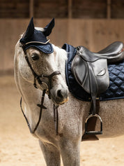 Side view of a gray horse wearing the navy PS of Sweden Heart Jump Pad under a brown saddle